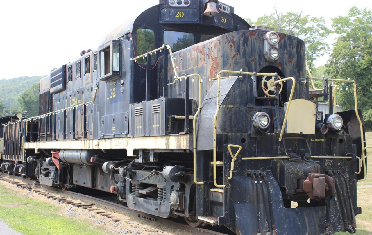 A weathered railroad locomotive parked in a park. It is painted in the black and yellow livery of the Lake Champlain & Moriah Railroad.